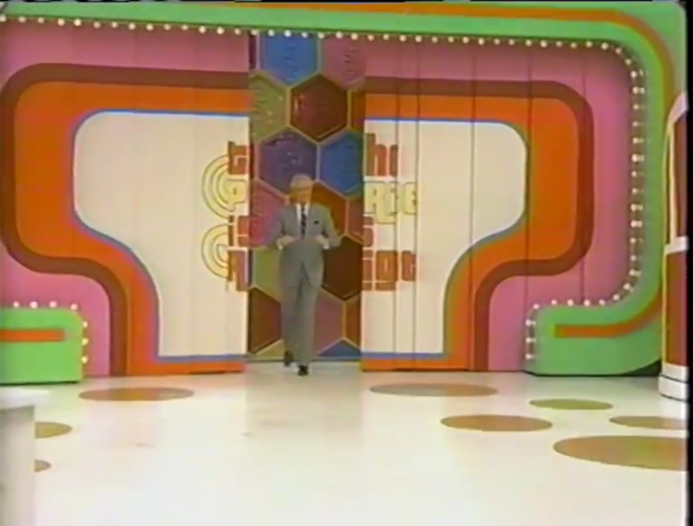A host walks through a colorful set on a game show, featuring vibrant backdrop designs and bright lights.