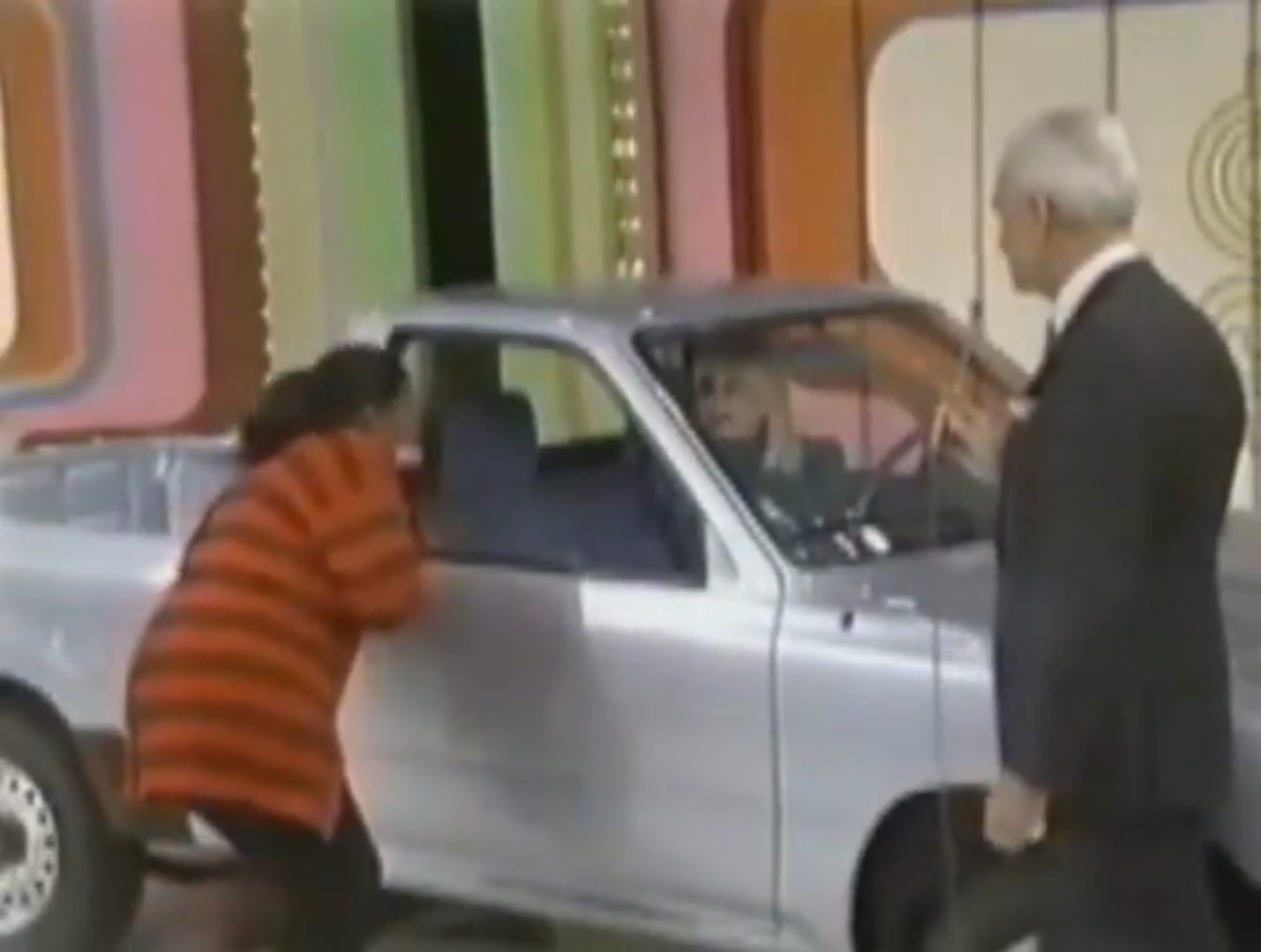 Cathy leans into a silver car on stage during a game show, while Bob Barker speaks to her.