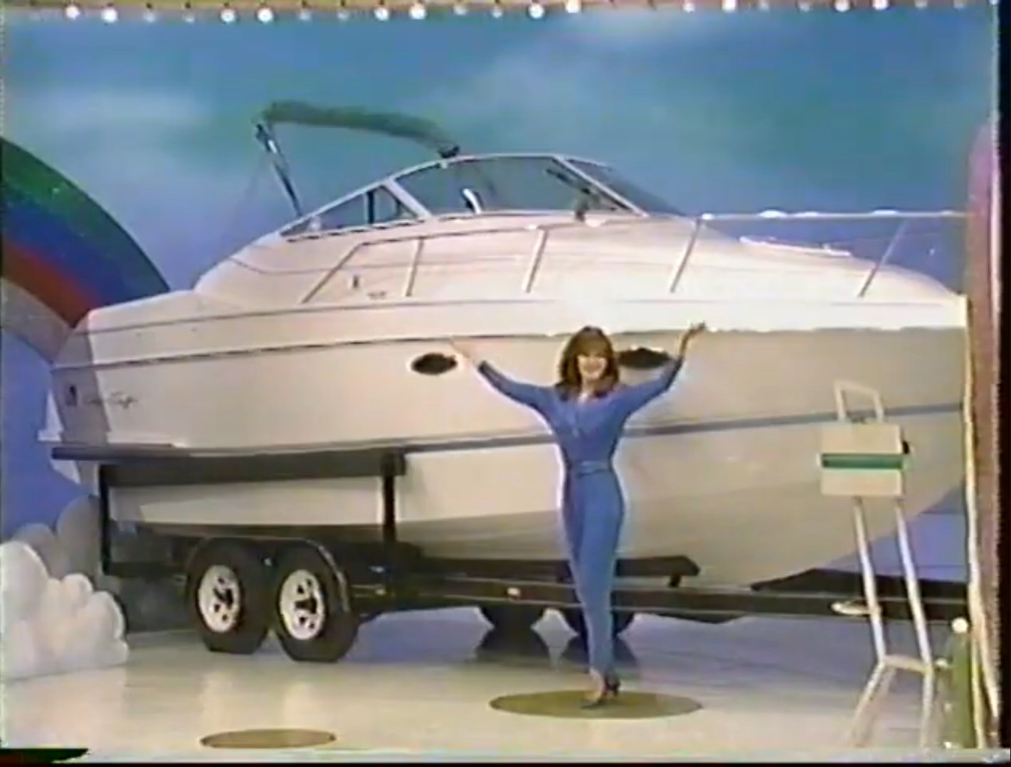 A model showcases a luxury boat on a stage with a colorful rainbow backdrop.