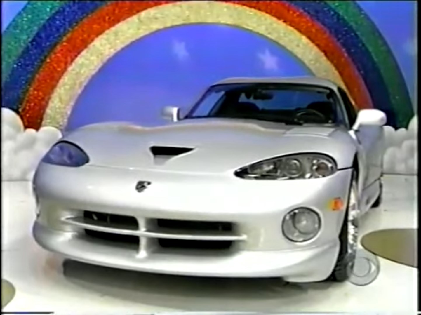 A silver Dodge Viper sports car displayed in front of a colorful rainbow backdrop, featuring fluffy cloud props.