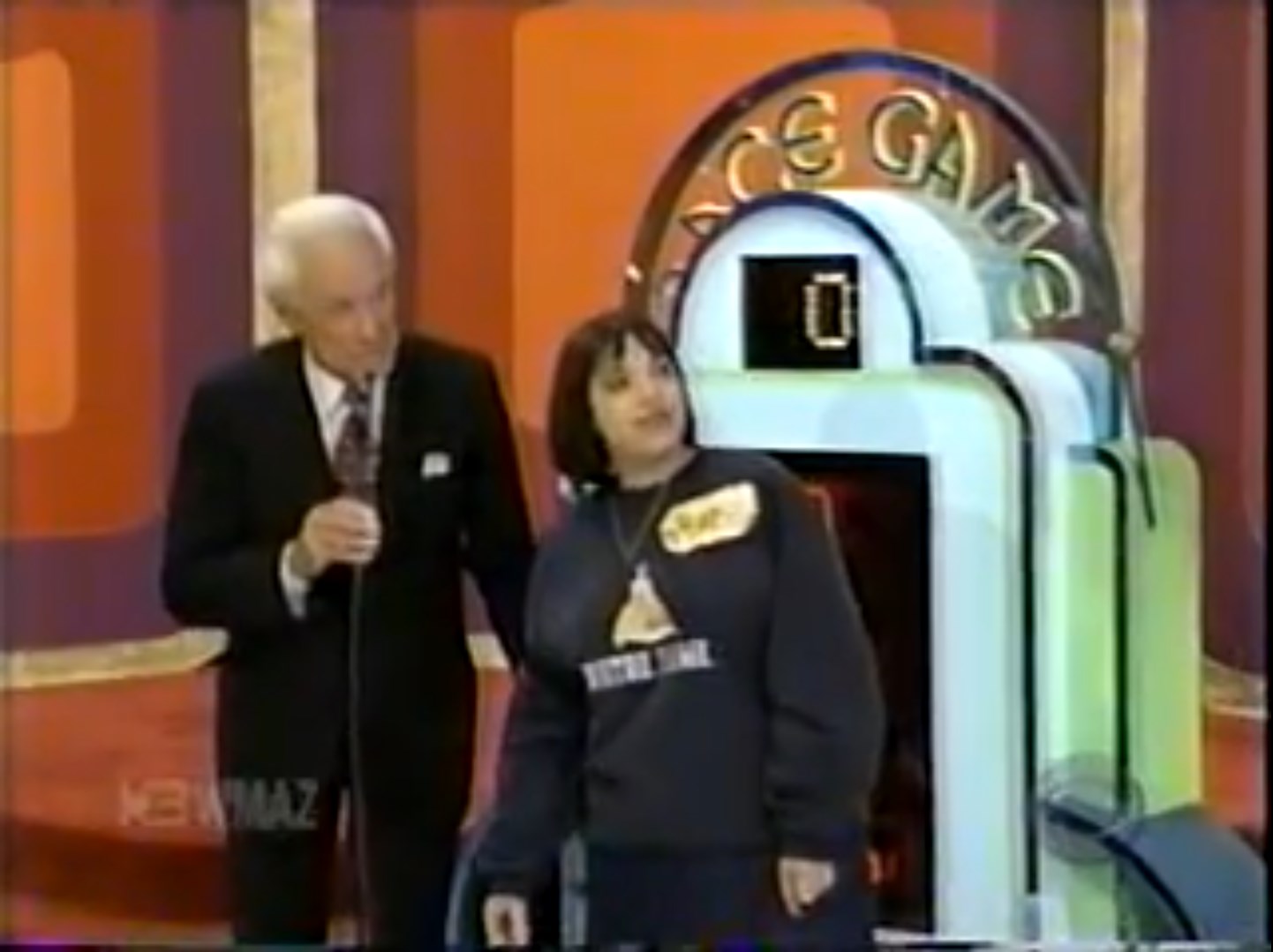 A contestant stands beside the host of The Price is Right, preparing to play the Race Game, with the game set visible in the background.