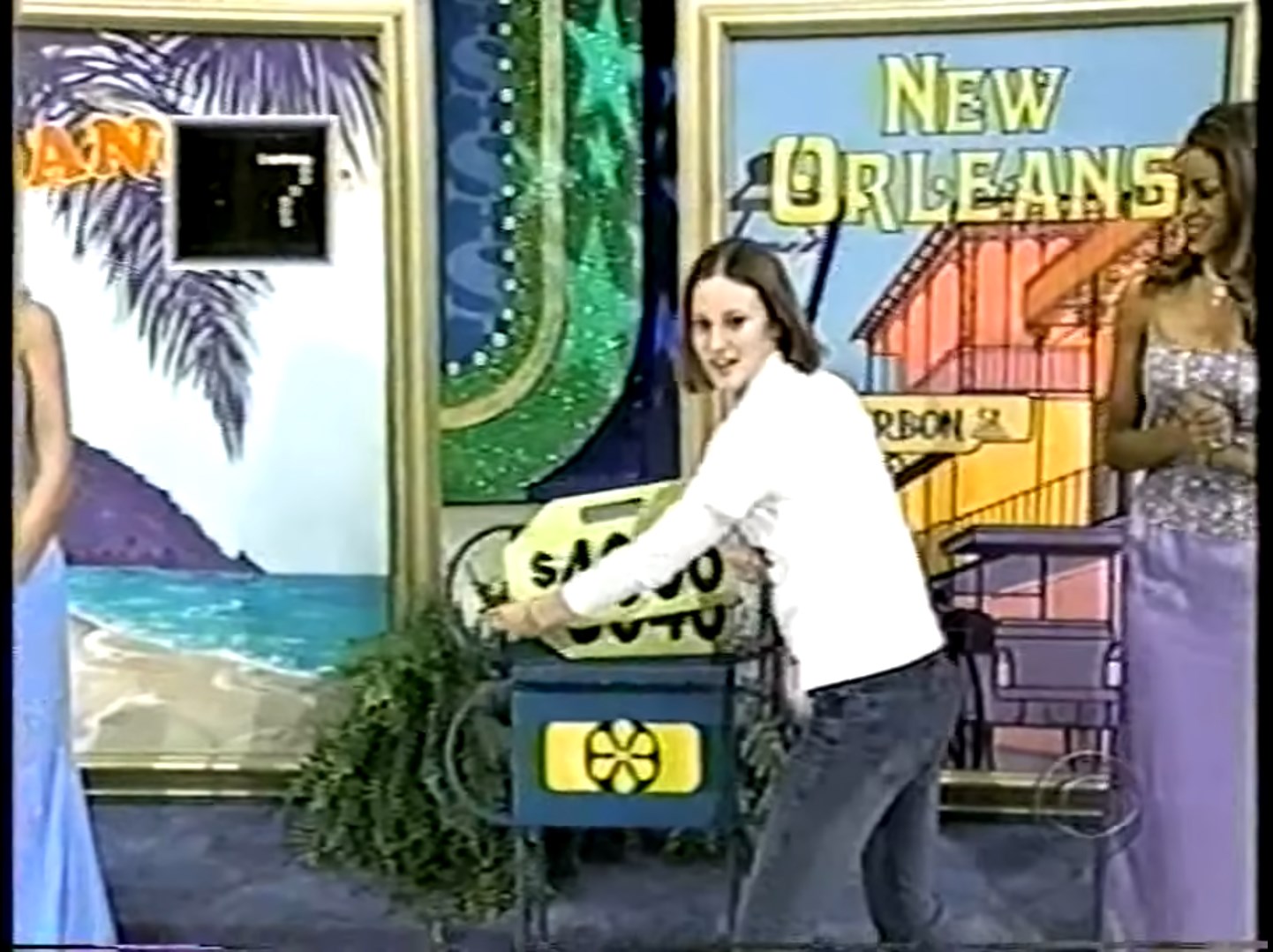 A contestant is playing a game onstage, holding a ,000 price tag while standing next to a display with a beach and a vibrant 'New Orleans' sign in the background.