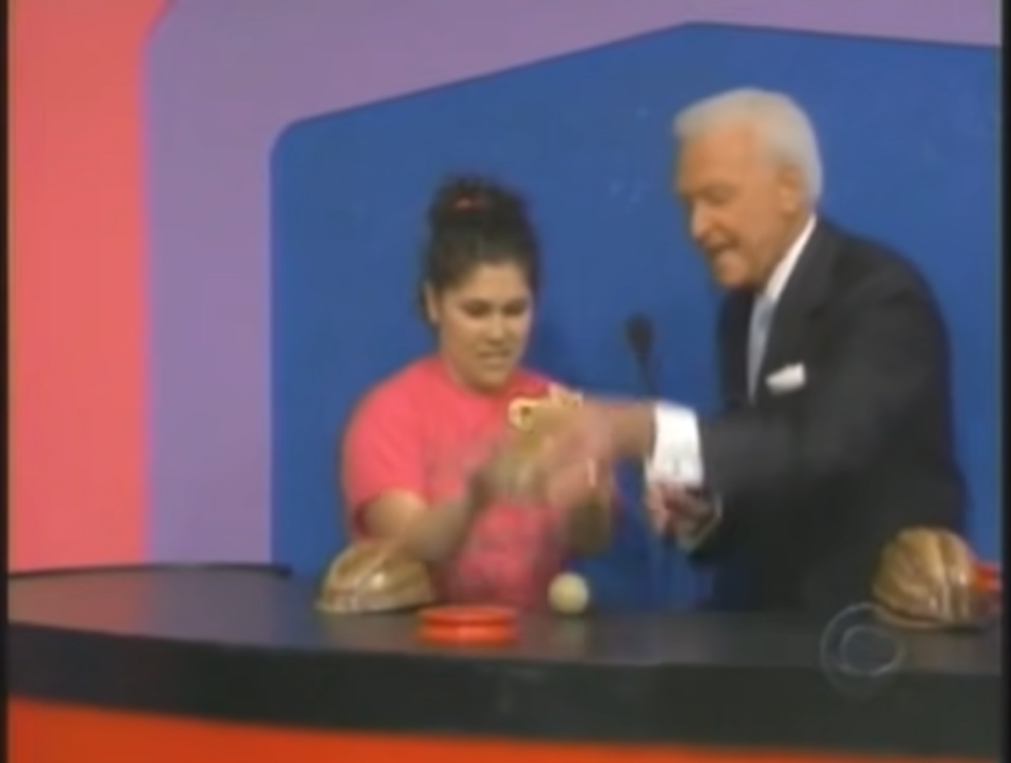 A contestant plays the Shell Game on The Price is Right, with the host mixing up three shells on a podium while the contestant focuses on the hidden ball.