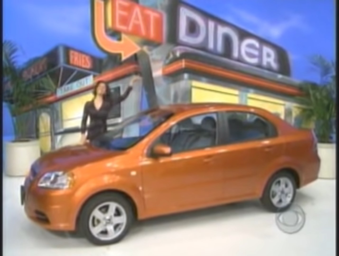 A contestant stands next to an orange car in front of a diner backdrop on The Price is Right set.