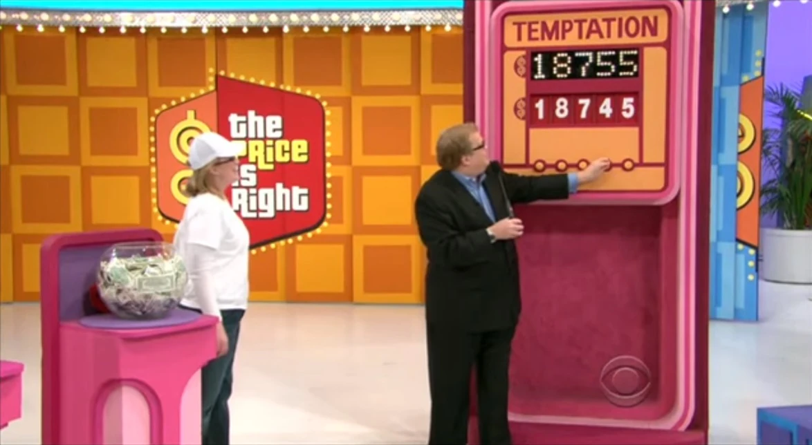 A game show host points at the price display for the Temptation game, featuring the numbers 18755 and 18745. Contestant stands nearby.