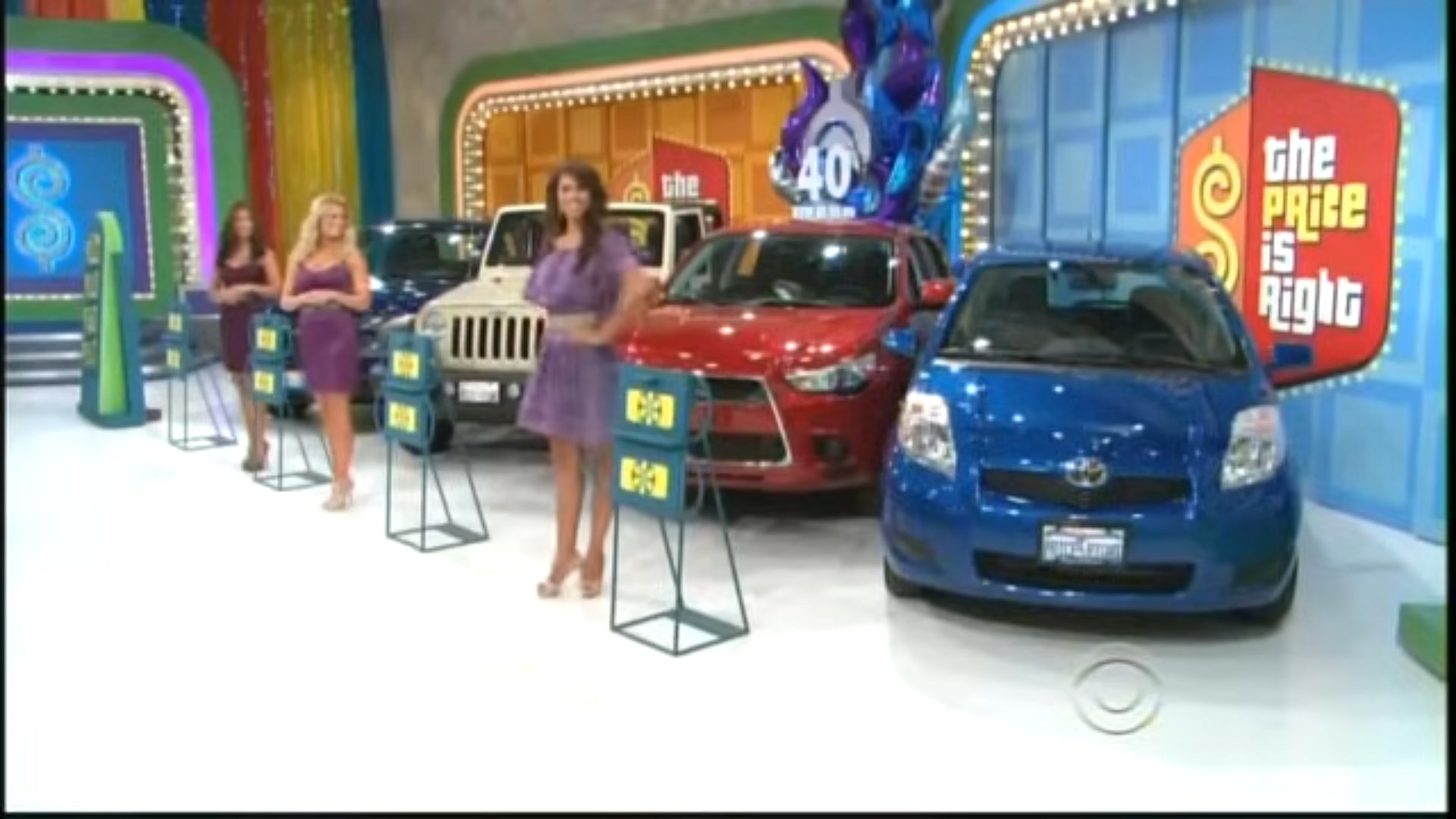 Four contestants stand beside various cars on the set of The Price is Right, celebrating the show's 40th anniversary.