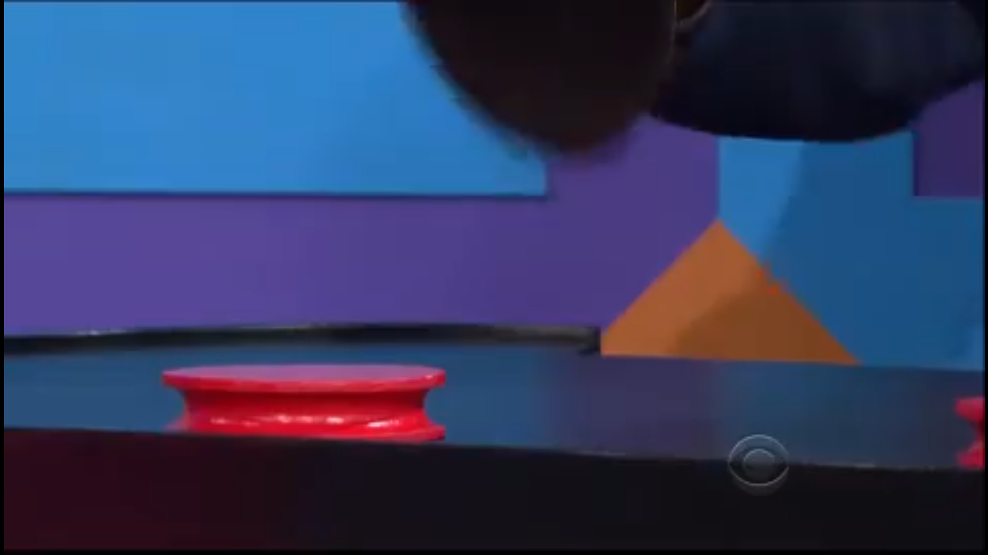 A close-up of a hand about to place a red chip on a black surface, possibly part of a game show setup.