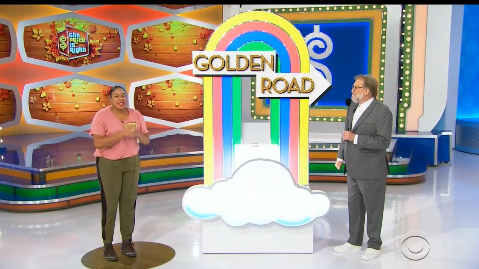 A contestant excitedly stands on stage next to the colorful 'Golden Road' sign during a game show.