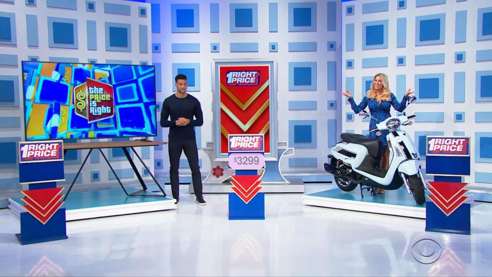 A game show set featuring the 'One Right Price' game with a large screen displaying the show's logo, a male presenter standing beside a prize display, and a female model showcasing a white scooter. The price tag shown is 99.