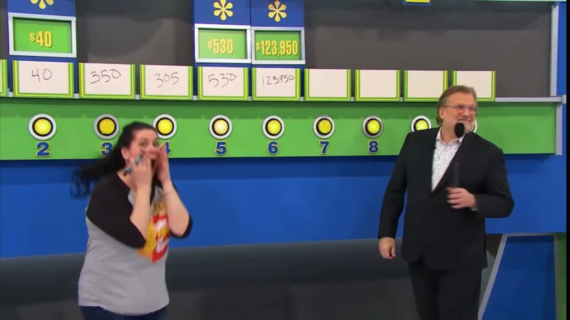 A contestant celebrates excitedly while standing next to a game board with various price options on display during a car game segment of The Price is Right.