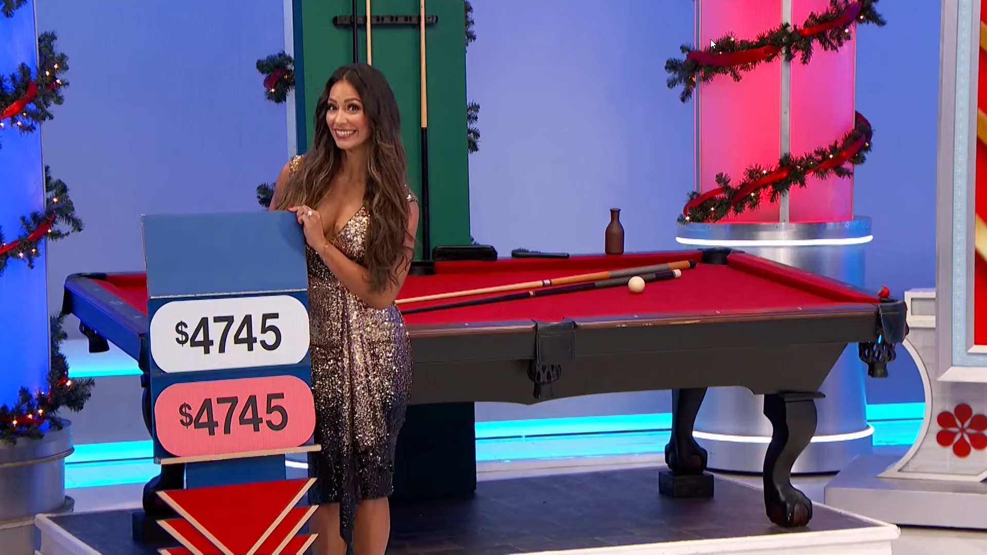 A model is smiling and holding a price tag of 45, next to a pool table decorated for the holidays.