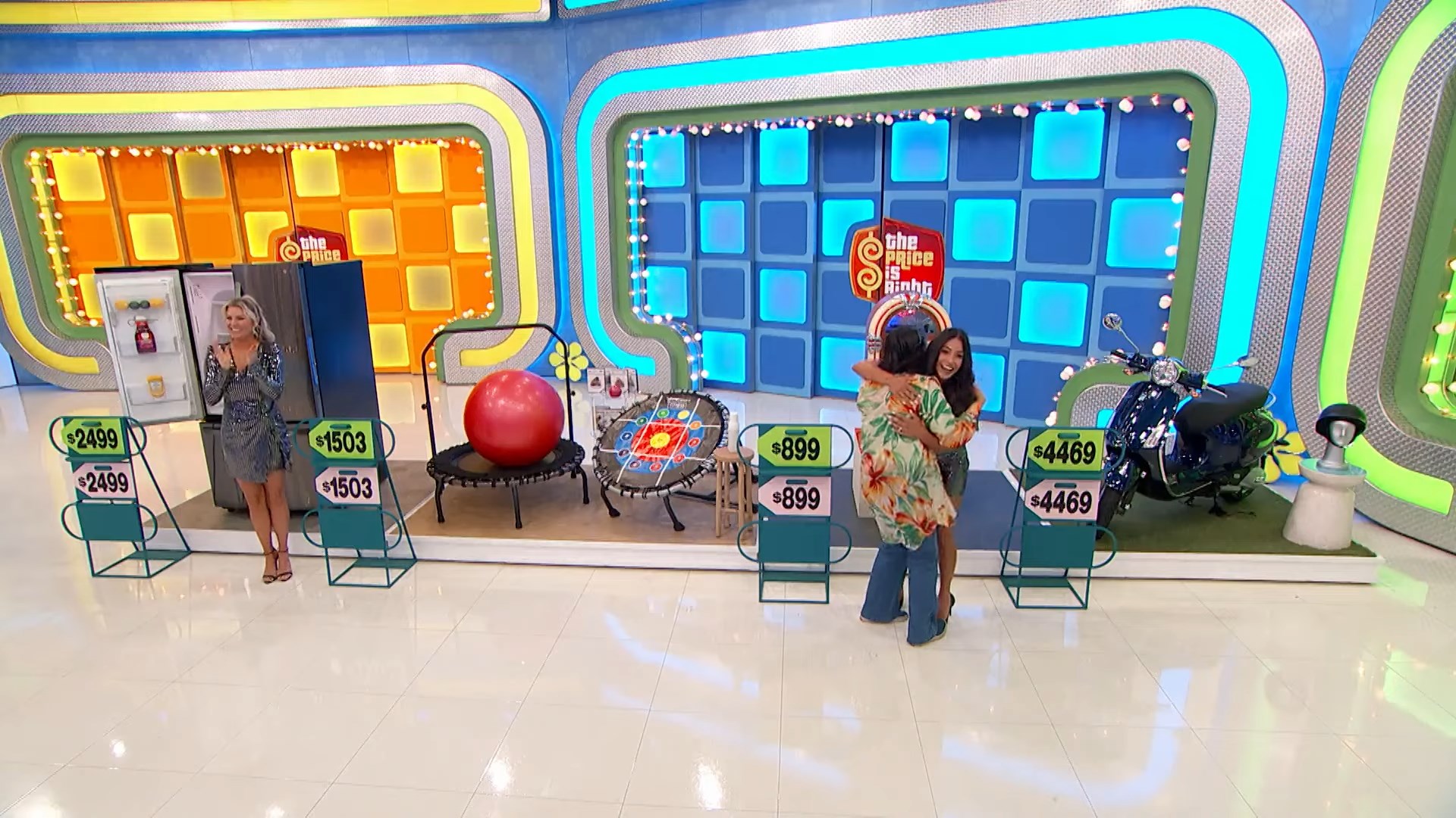 Contestants celebrate on The Price is Right stage, showcasing various prizes with price tags, including a trampoline and a motorcycle.