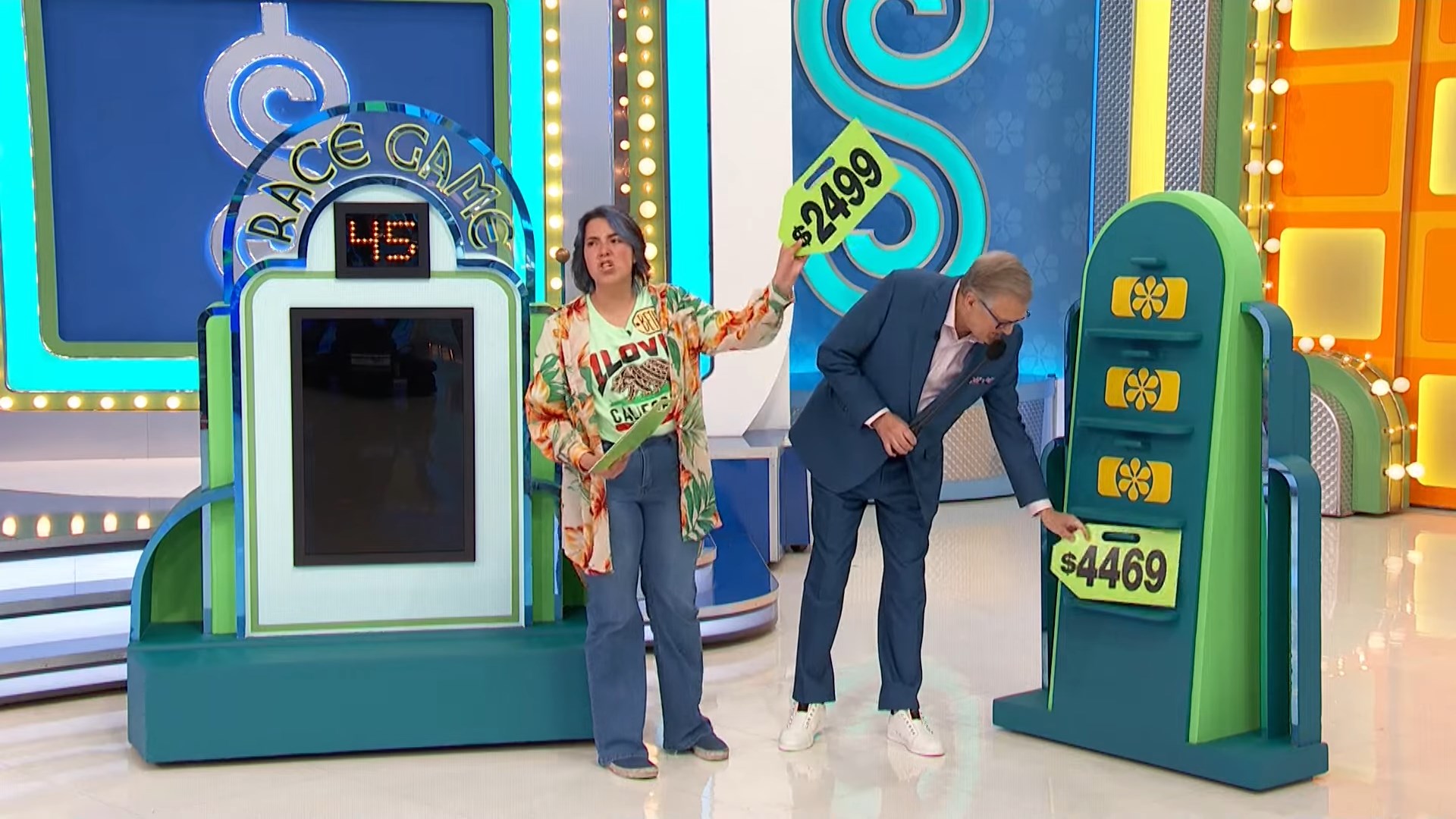 Contestant holding a price tag at the Race Game on The Price is Right, while the host adjusts the pricing display.