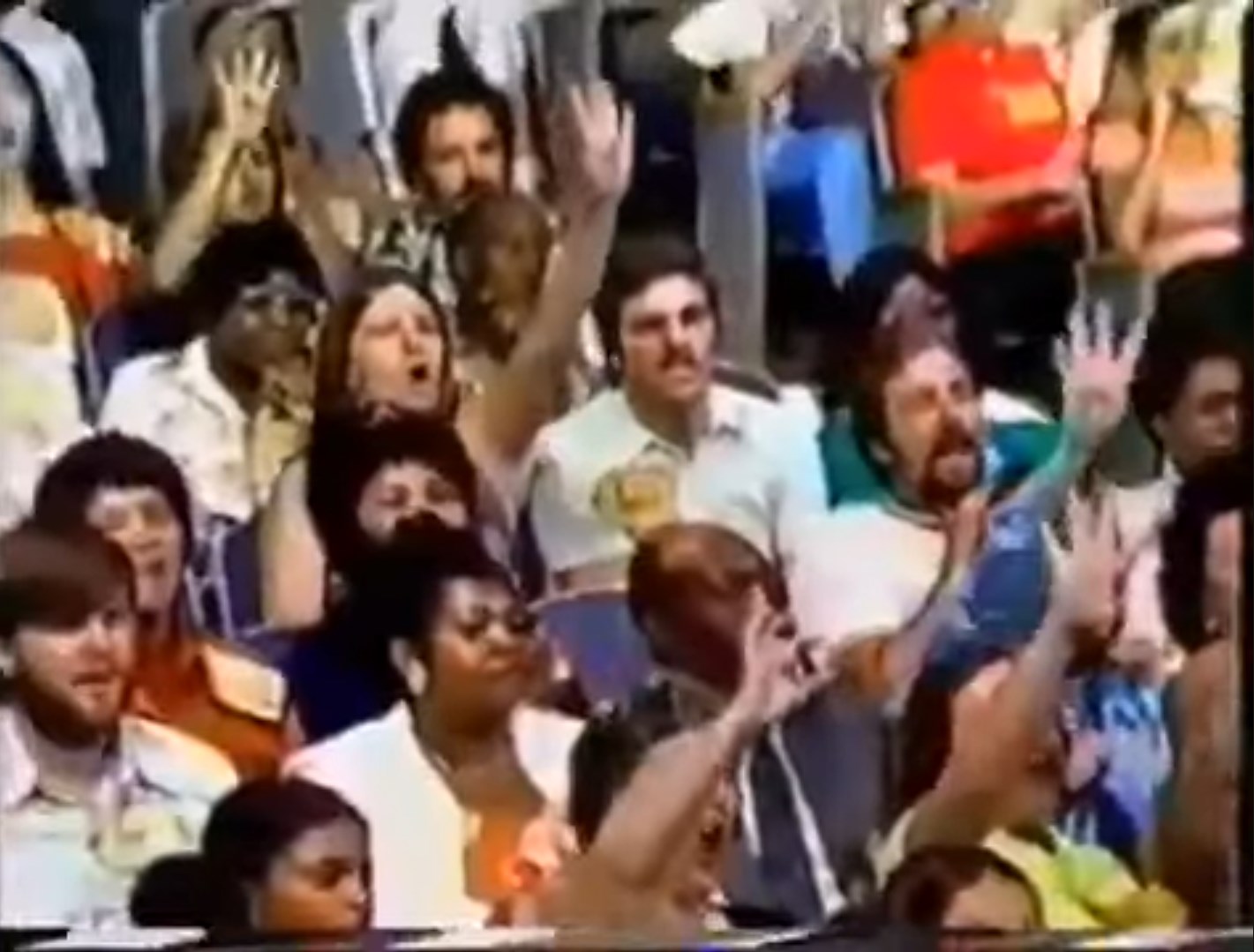 Audience members are enthusiastically raising their hands while watching a game show, showcasing excitement and engagement.
