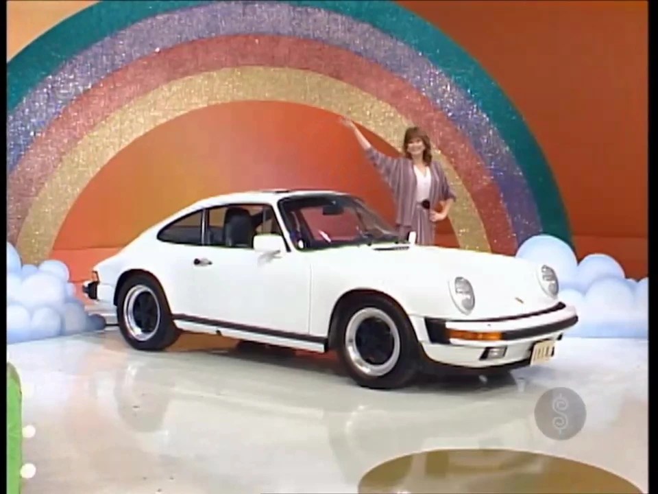 A woman stands next to a white Porsche sports car in front of a colorful rainbow backdrop, promoting the Golden Road game show segment.