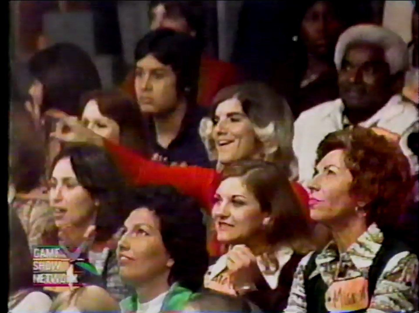 Audience members reacting excitedly during a game show segment, with several women in close view wearing name tags.