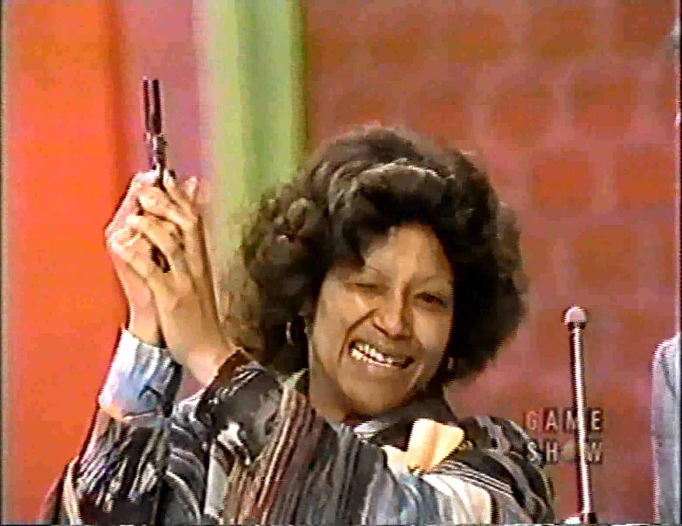 A contestant holds up a starter pistol, smiling, during a game show segment.