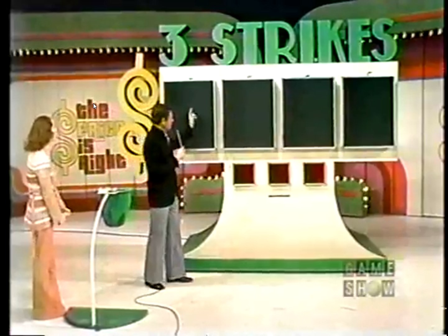 Host pointing at the Three Strikes game board on The Price is Right, with a female contestant watching.
