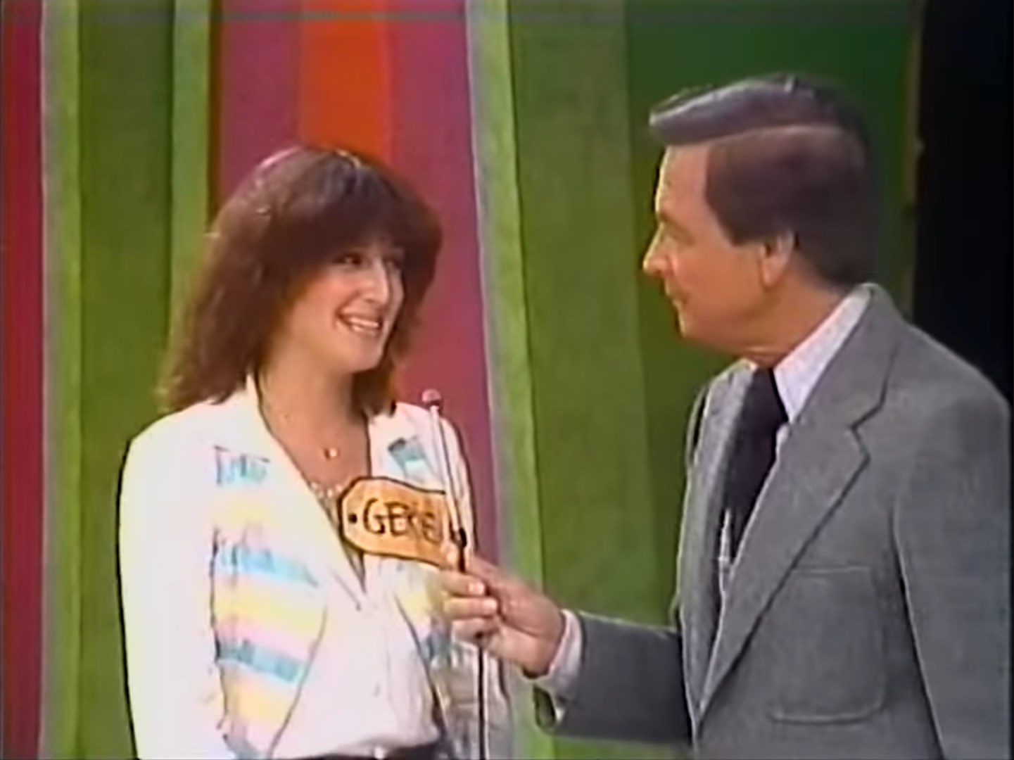 A contestant named Gerie smiles while holding a microphone during a segment of The Price is Right, with colorful background and host Bob Barker engaging with her.