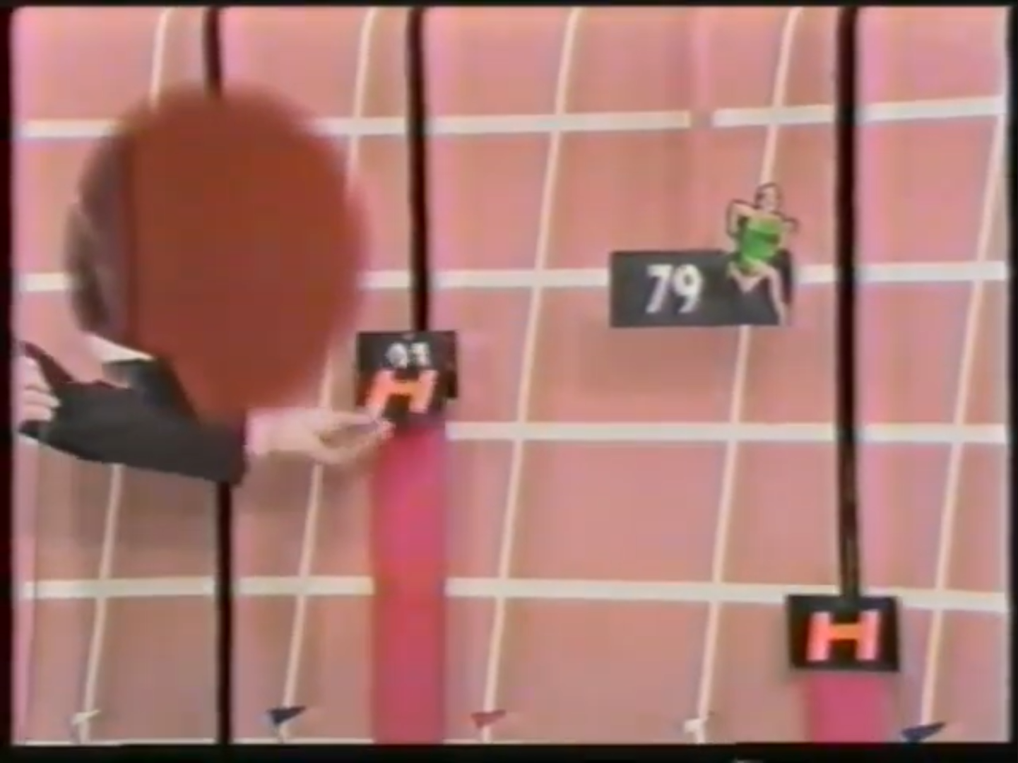A scene from the game show 'The Price is Right' featuring a visual of a cartoon runner on a track with hurdles, while a hand is placing a marker on a scoreboard.