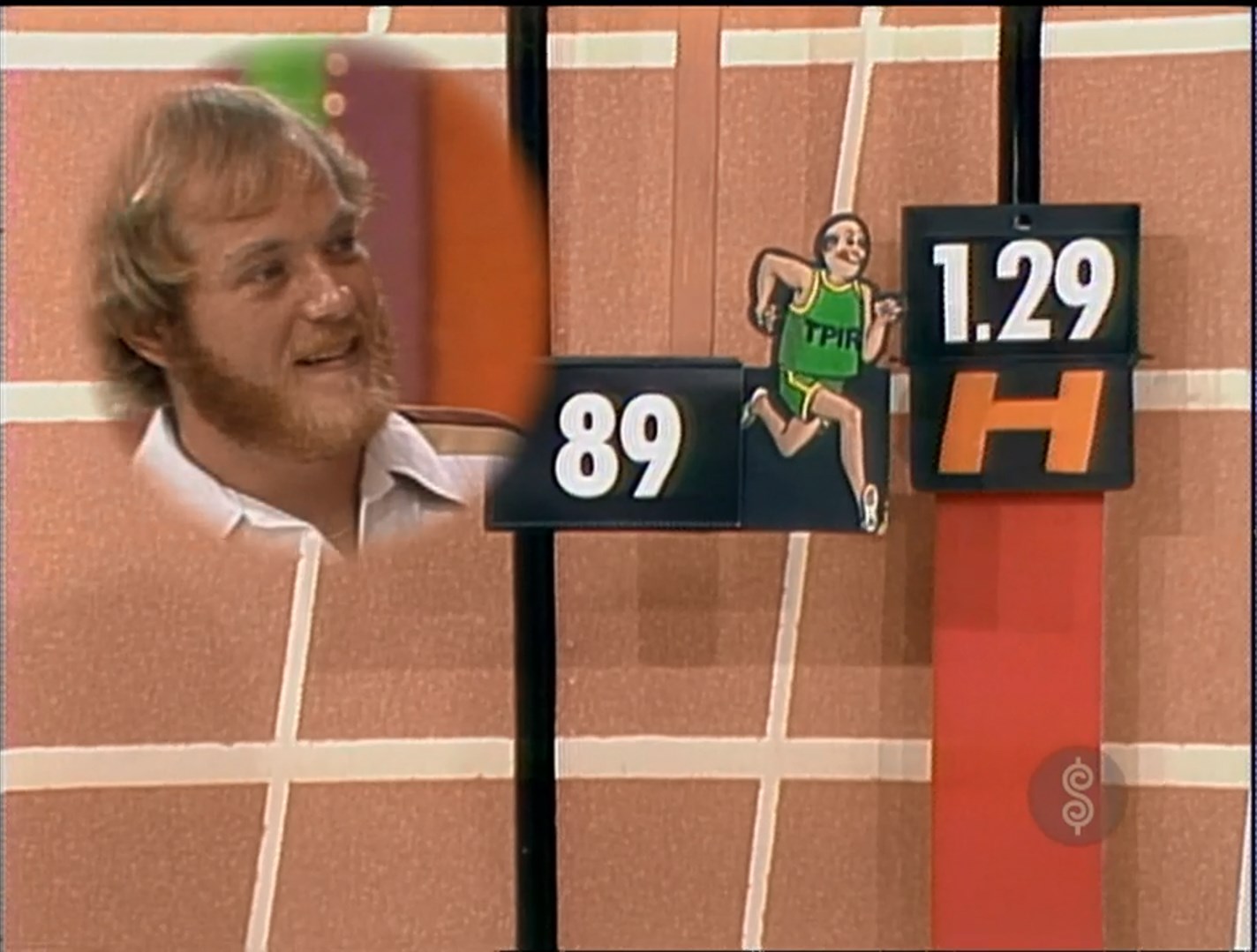 A contestant with a beard smiles while looking at a scoreboard featuring a cartoon runner and prices during a game on The Price is Right.