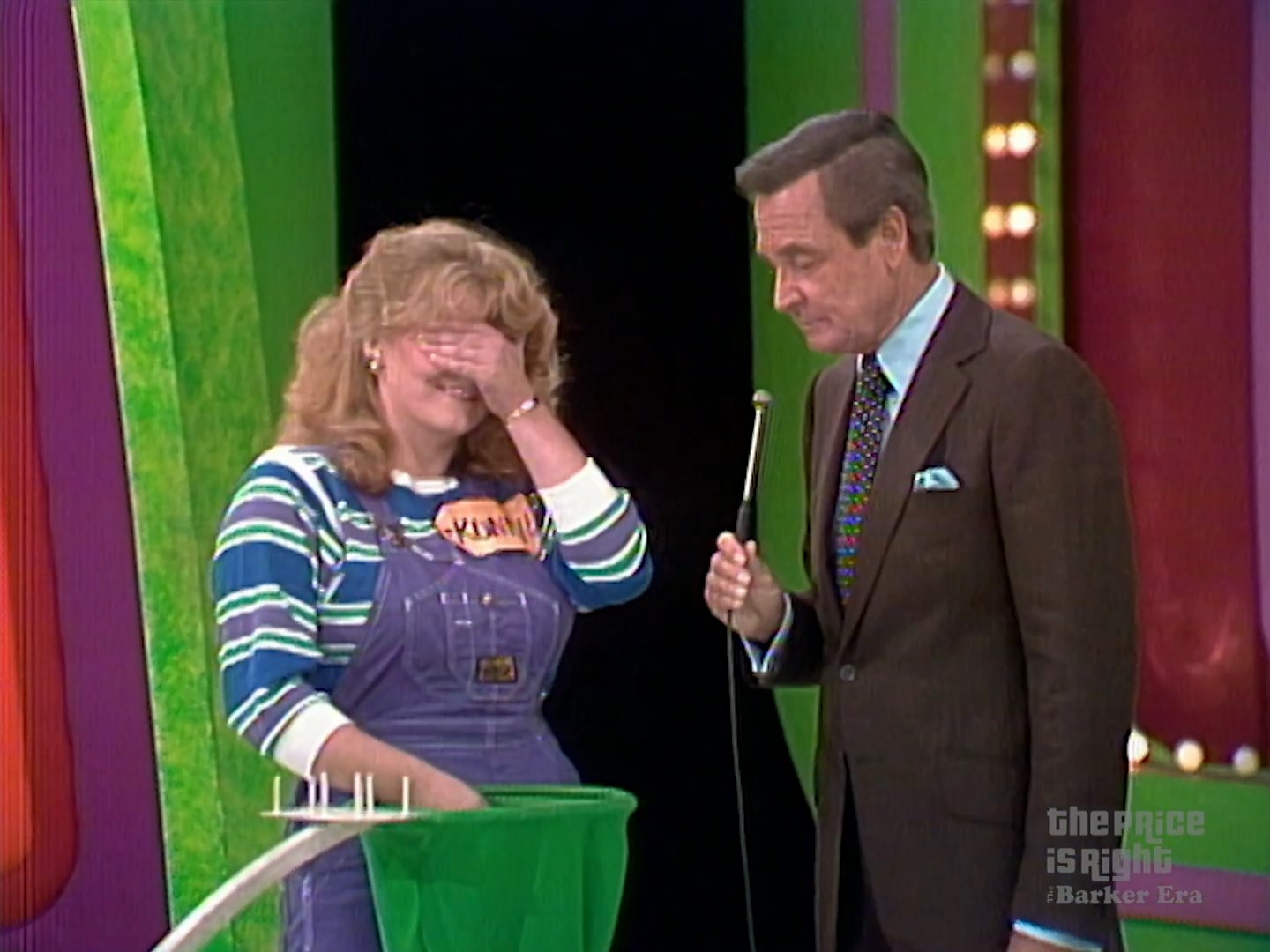A contestant on The Price is Right covers her eyes while Bob Barker asks a question, with a colorful backdrop emphasizing the show's vibrant set.