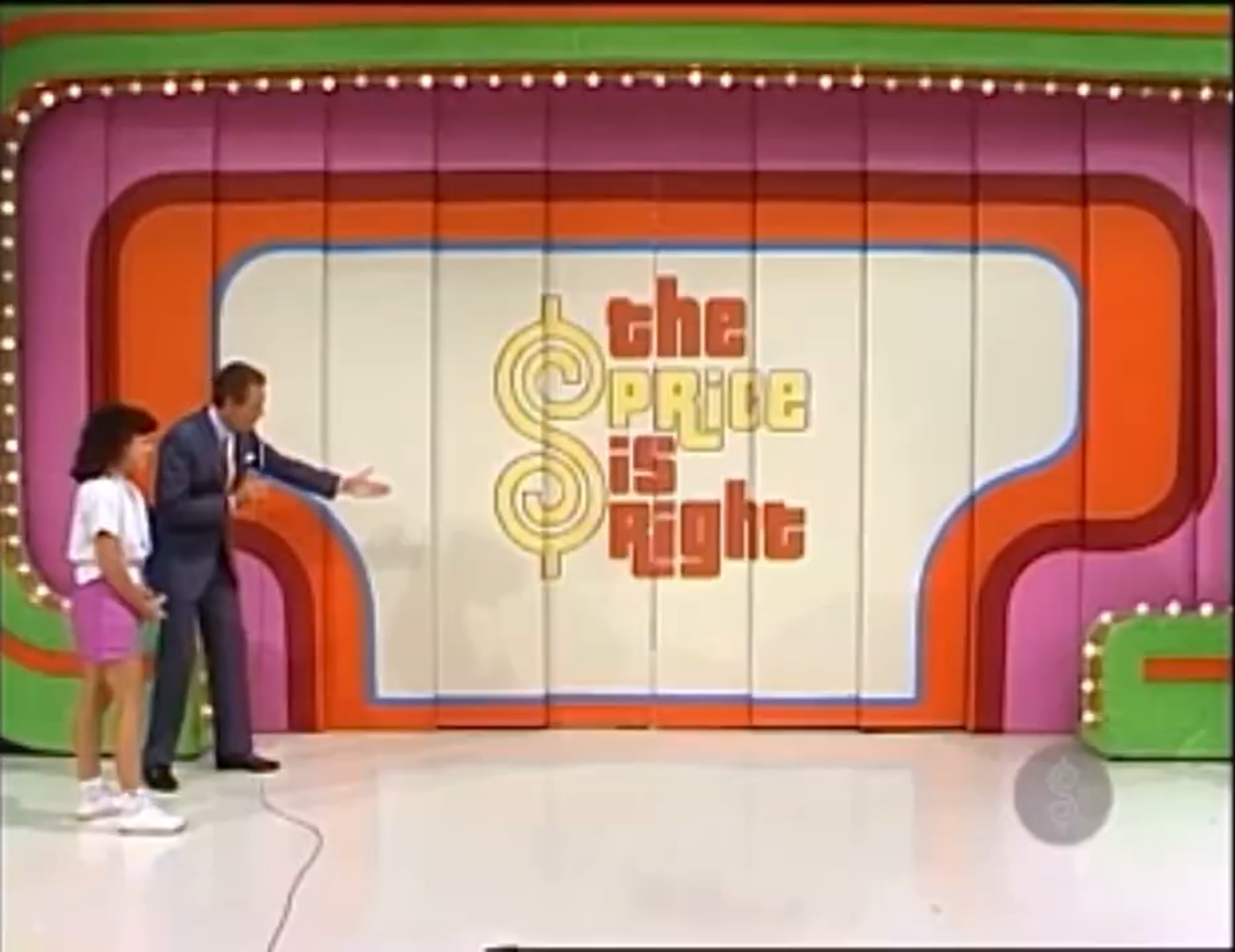 A scene from 'The Price Is Right' featuring a host and a contestant in front of the show's colorful backdrop.