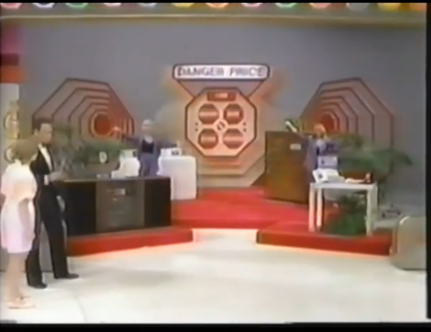 A scene from the game show 'The Price Is Right' featuring the 'Danger Price' game setup, with contestants and hosts participating in front of a colorful backdrop and prize displays.