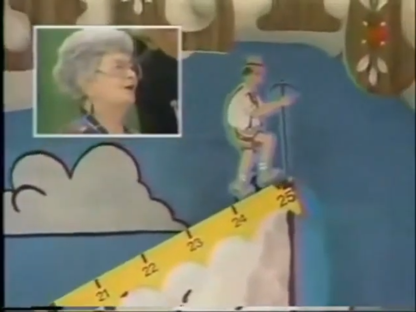 A cartoon mountain climber ascends a cliff marked with steps from 0 to 25, while a contestant reacts in a smaller inset photo.