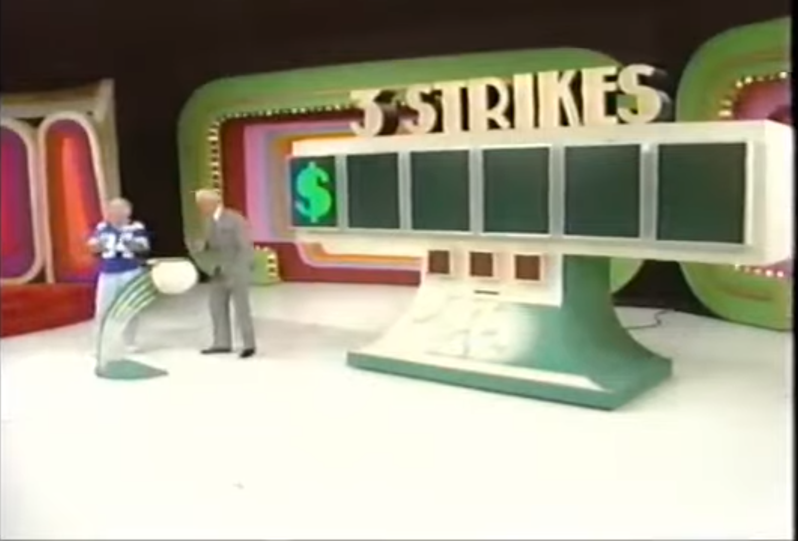 A contestant prepares to play the 'Three Strikes' game on 'The Price is Right', holding a ball while the host stands beside a large game board with $ and empty slots for digits.