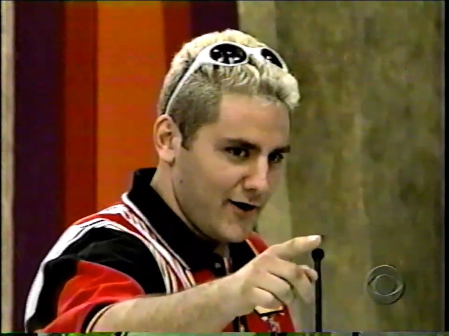 A contestant from The Price is Right, wearing a red and black shirt, points while engaging with the audience.