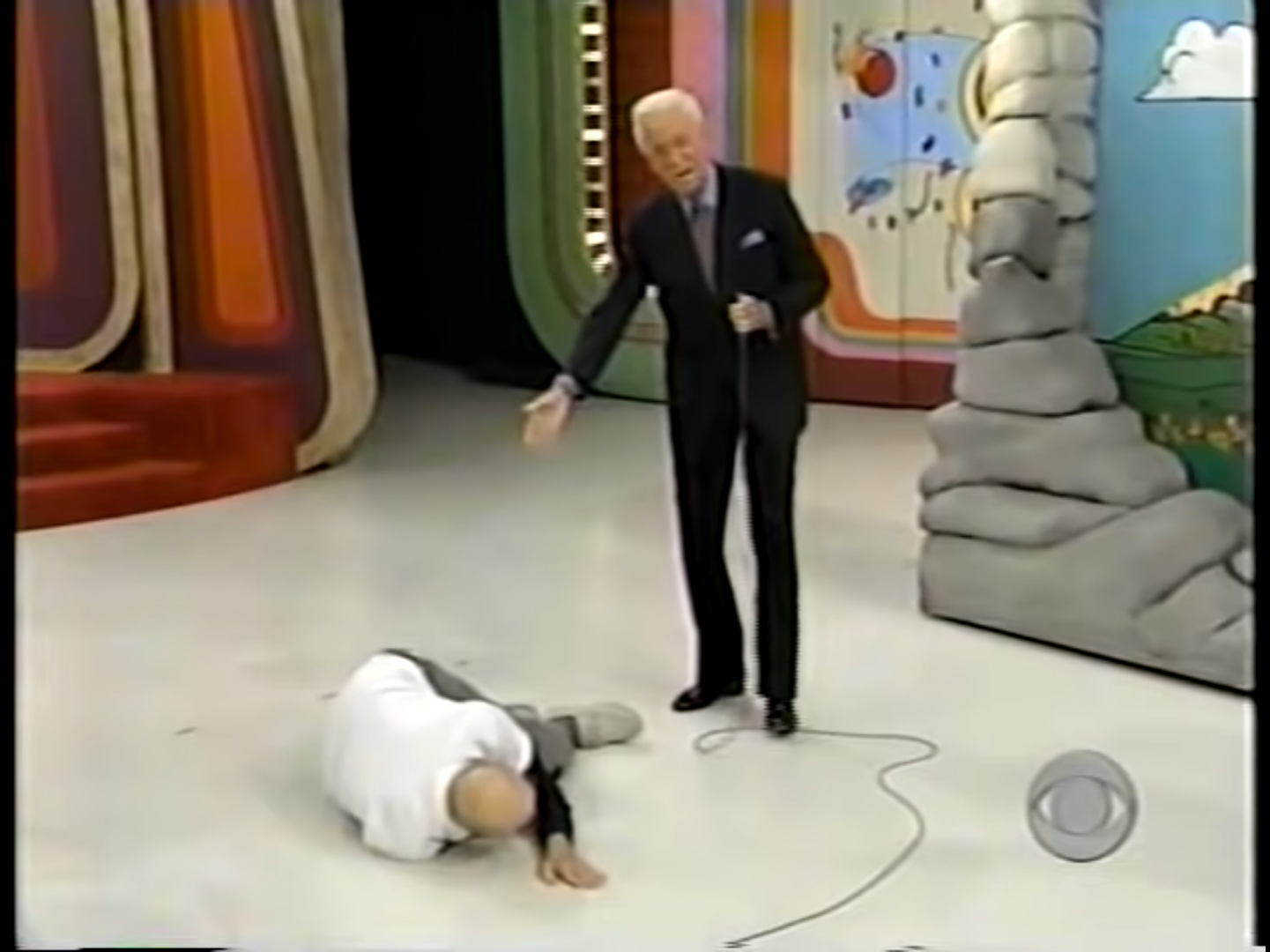 Bob Barker helping a contestant on The Price is Right, with the contestant lying on the floor.