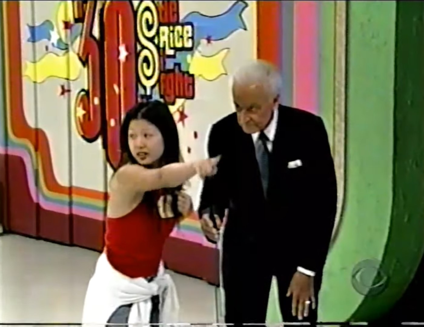 A contestant gestures while speaking to the host during a game segment, with colorful background graphics displaying '30' and 'Price is Right' in a studio setting.