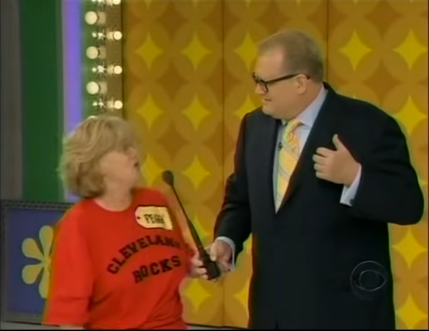 A contestant wearing a 'CLEVELAND ROCKS' t-shirt enthusiastically interacts with the host, Drew Carey, on stage at The Price is Right.