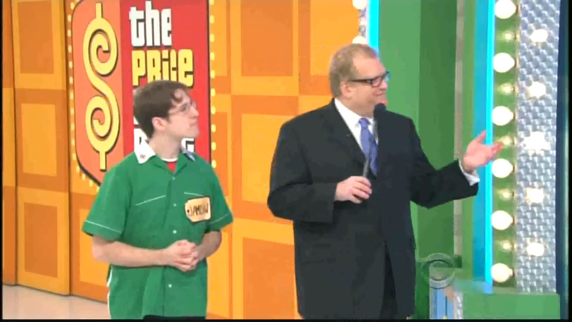 Contestant and host on stage during the game show 'The Price Is Right', with colorful prize display behind them.