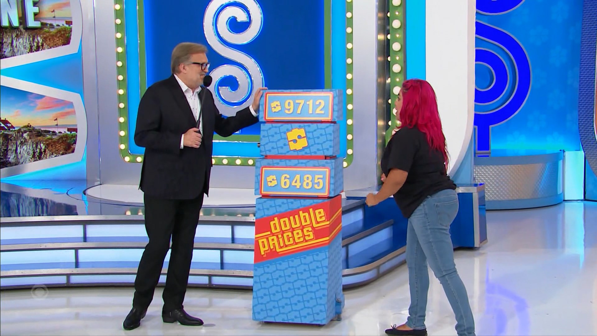 Drew Carey points to two price tags for the game 'Double Prices', while a contestant with pink hair examines the options.