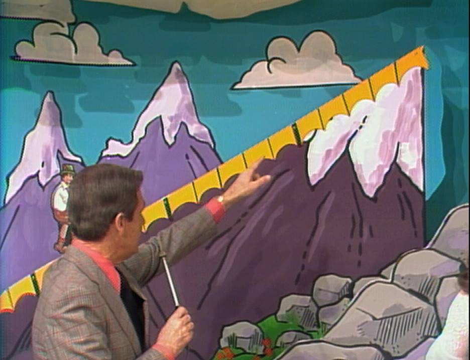 A host pointing to a colorful mountain backdrop featuring the iconic mountain climber from the game 'Cliff Hangers' on The Price is Right.