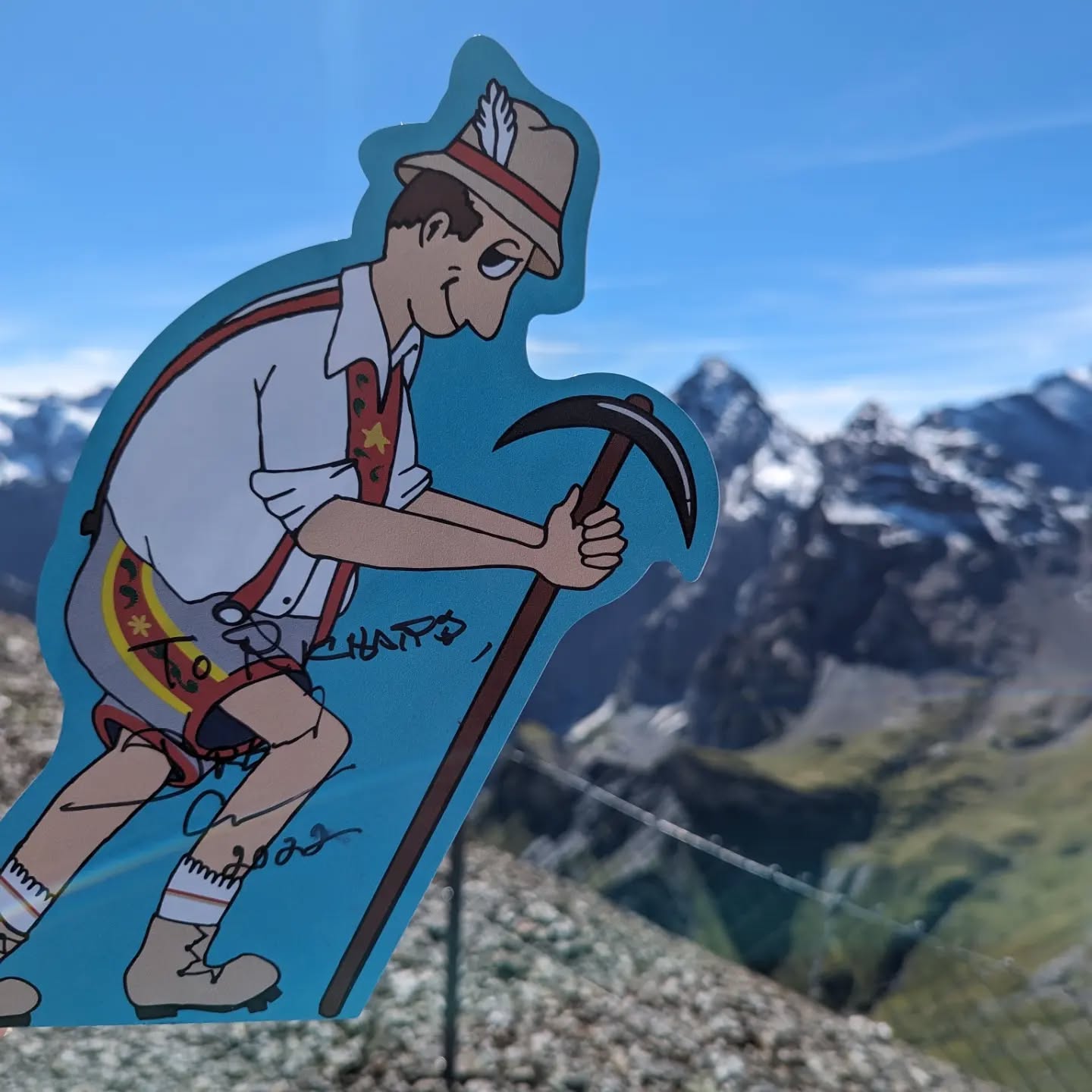 A cartoon mountain climber figure, dressed in traditional alpine attire, holds a pickaxe while standing on a rocky surface with a mountainous background.