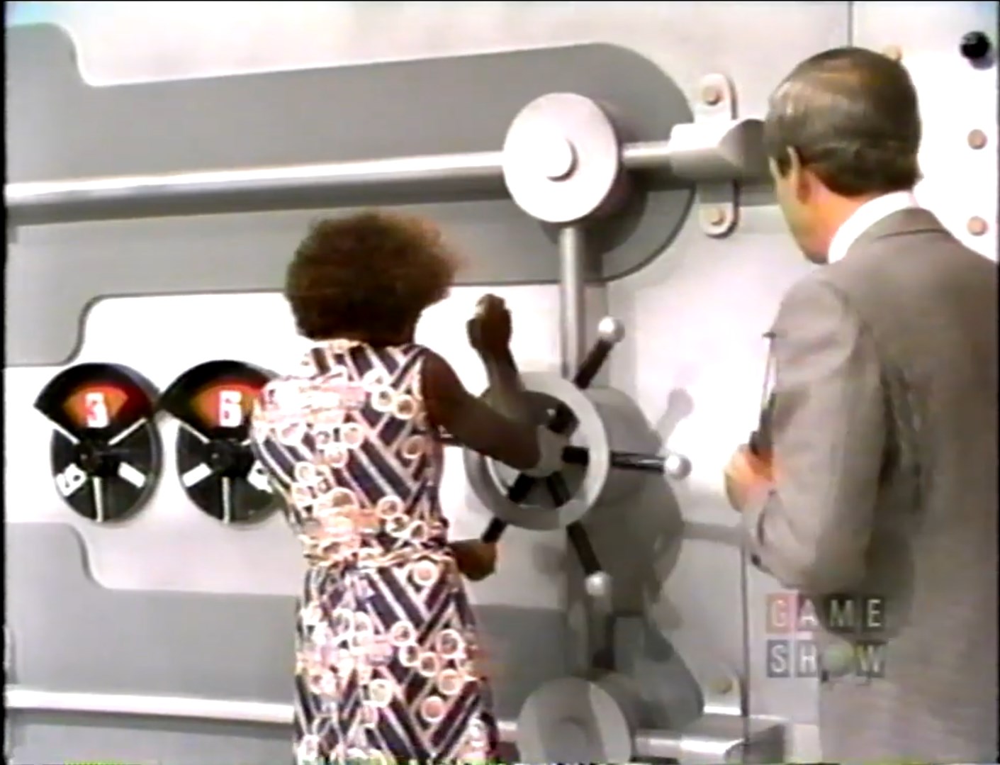 Contestant dialing the combination on a large game show safe, while the host observes.