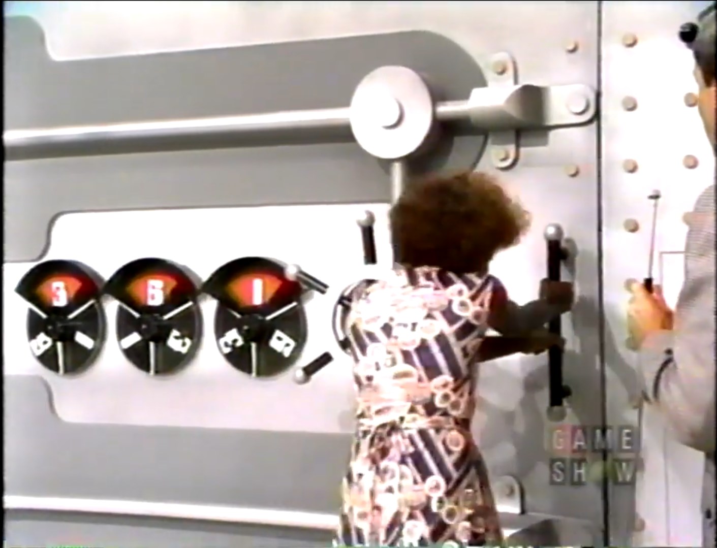 A contestant trying to open a large safe on a game show, with the combination dial showing the numbers 3, 6, and 1.