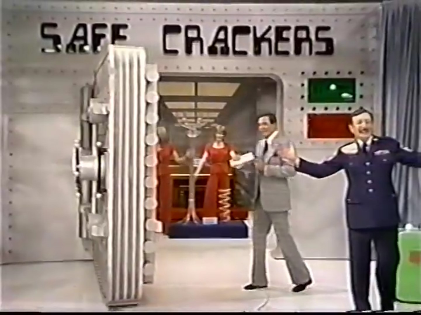 A large safe labeled 'SAFE CRACKERS' is open on a game show stage, with two hosts presenting the game while a female model stands nearby.
