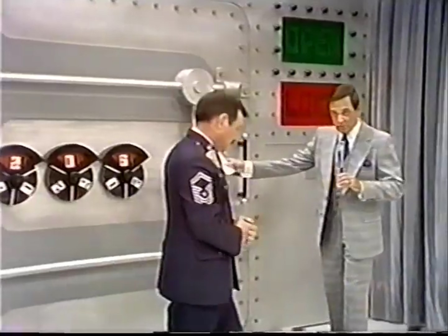 A game host explains the rules of Safe Crackers while a contestant turns the combination dials set to 205, with an 'OPEN' and 'LOCK' sign in the background.