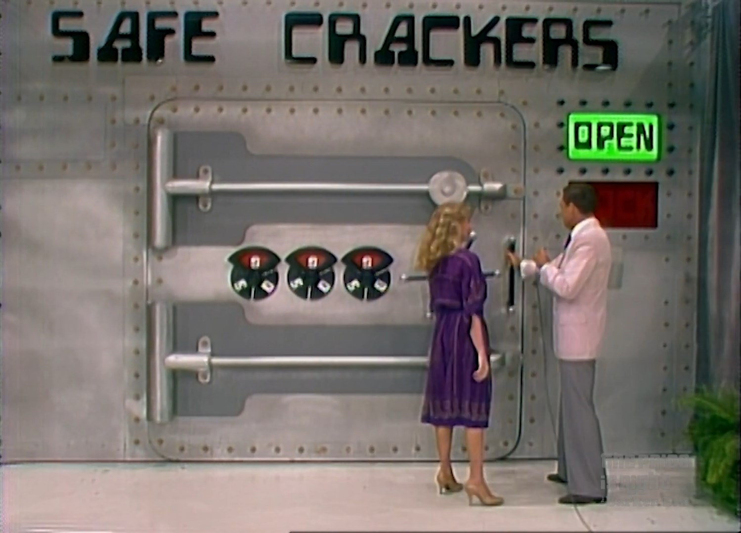 A contestant interacts with the host in front of the 'Safe Crackers' game on a television stage, with a large metallic safe displaying combination dials.