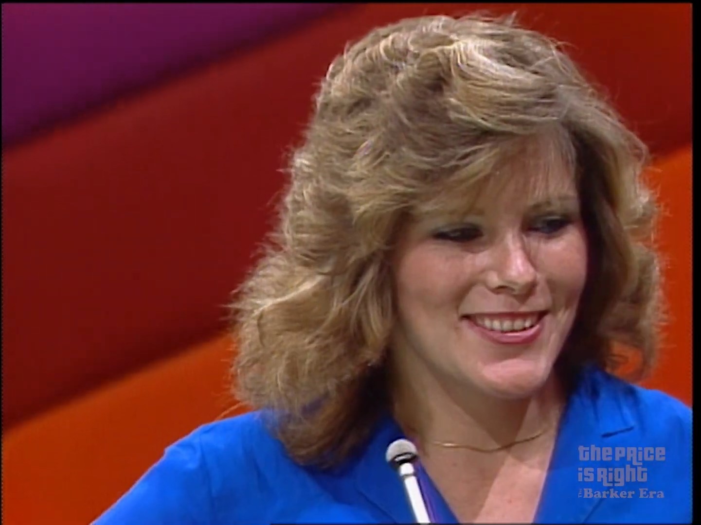 A contestant smiling during a game show segment, with colorful background elements.