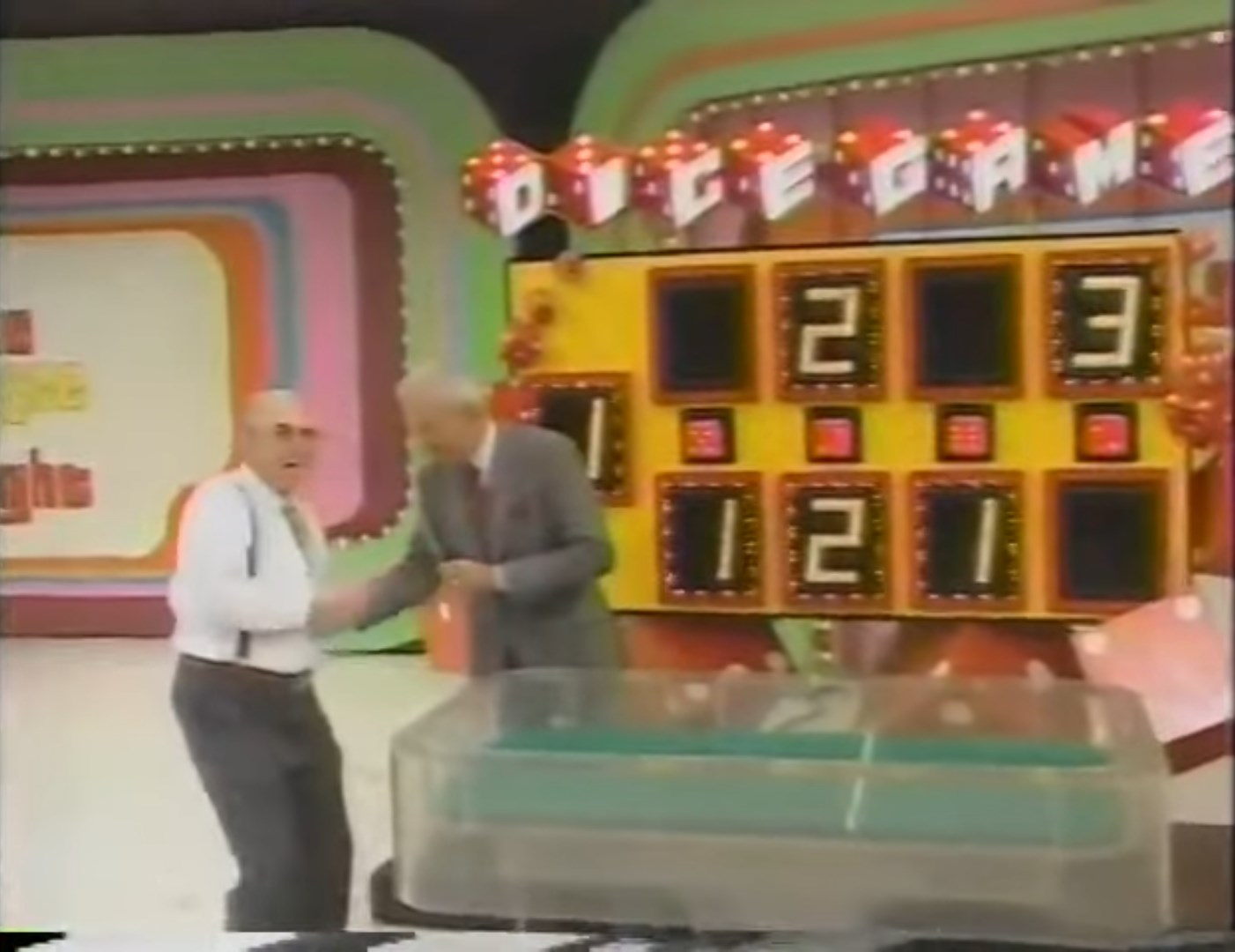 A contestant shakes hands with the host during the Dice Game, with a scoreboard displaying the numbers 2, 3, and 121 in the background.