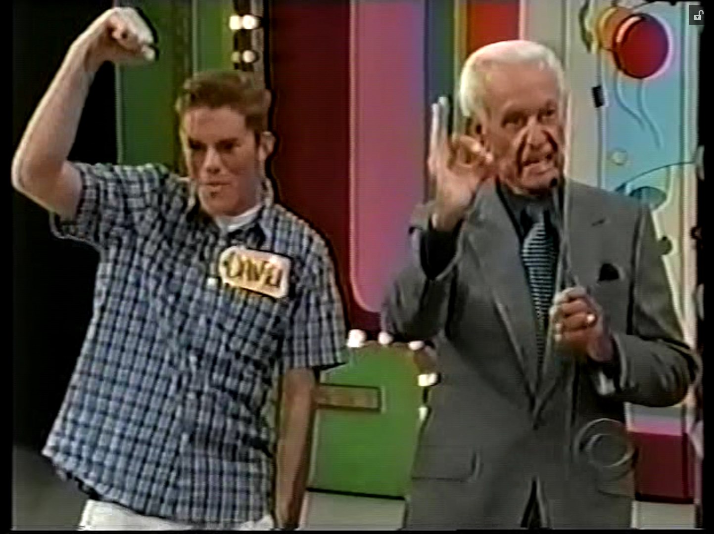 Daniel celebrating with a raised fist while standing next to the host of a game show, both appearing excited within a colorful game show set.