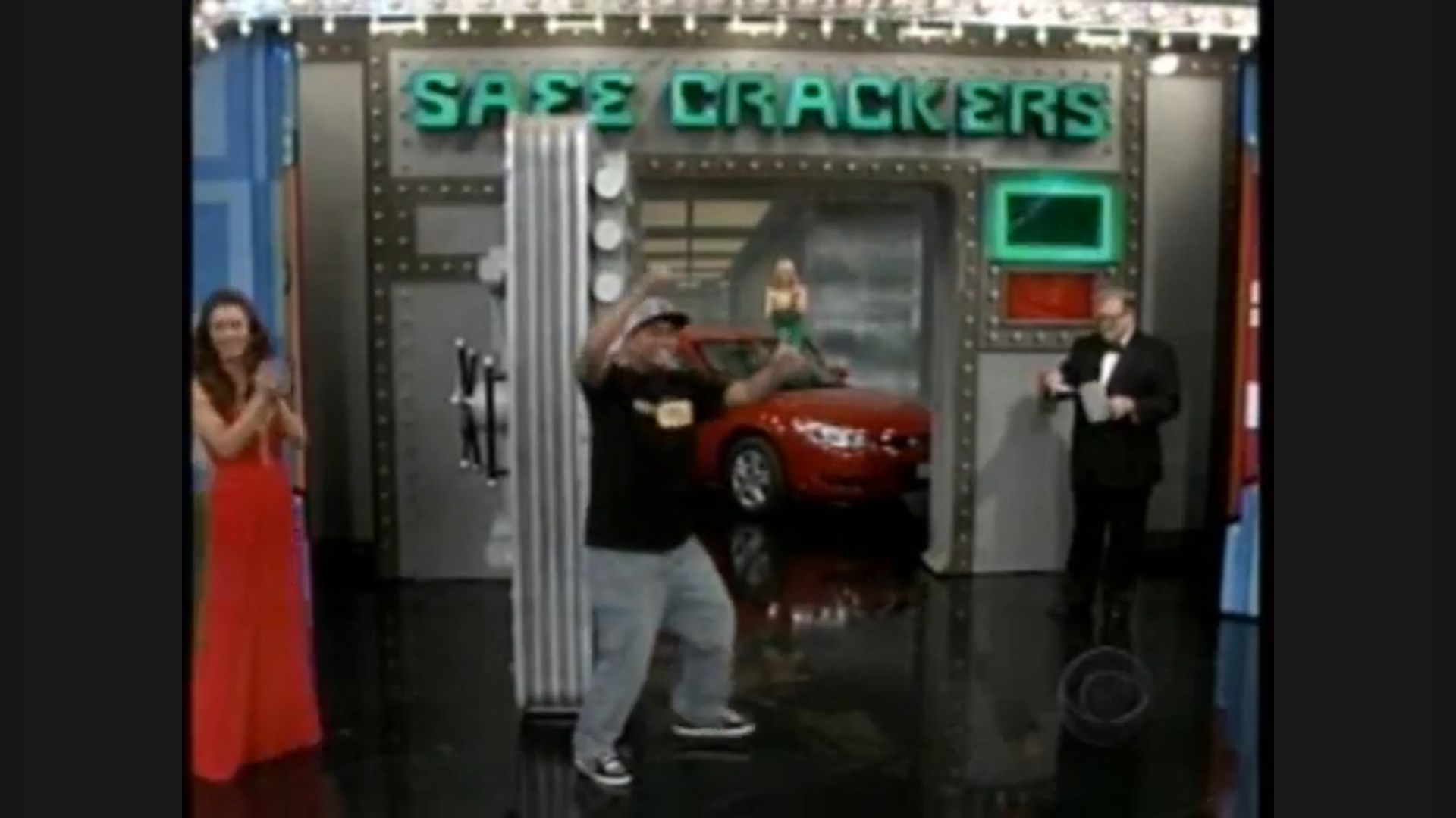 A contestant celebrates in front of the 'Safe Crackers' game show set on The Price is Right, with a red car visible in the background and a female model showcasing prizes.