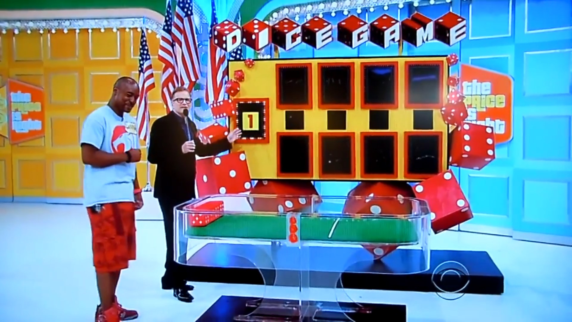 Contestant and host in front of the Dice Game board featuring oversized dice and hidden numbers.