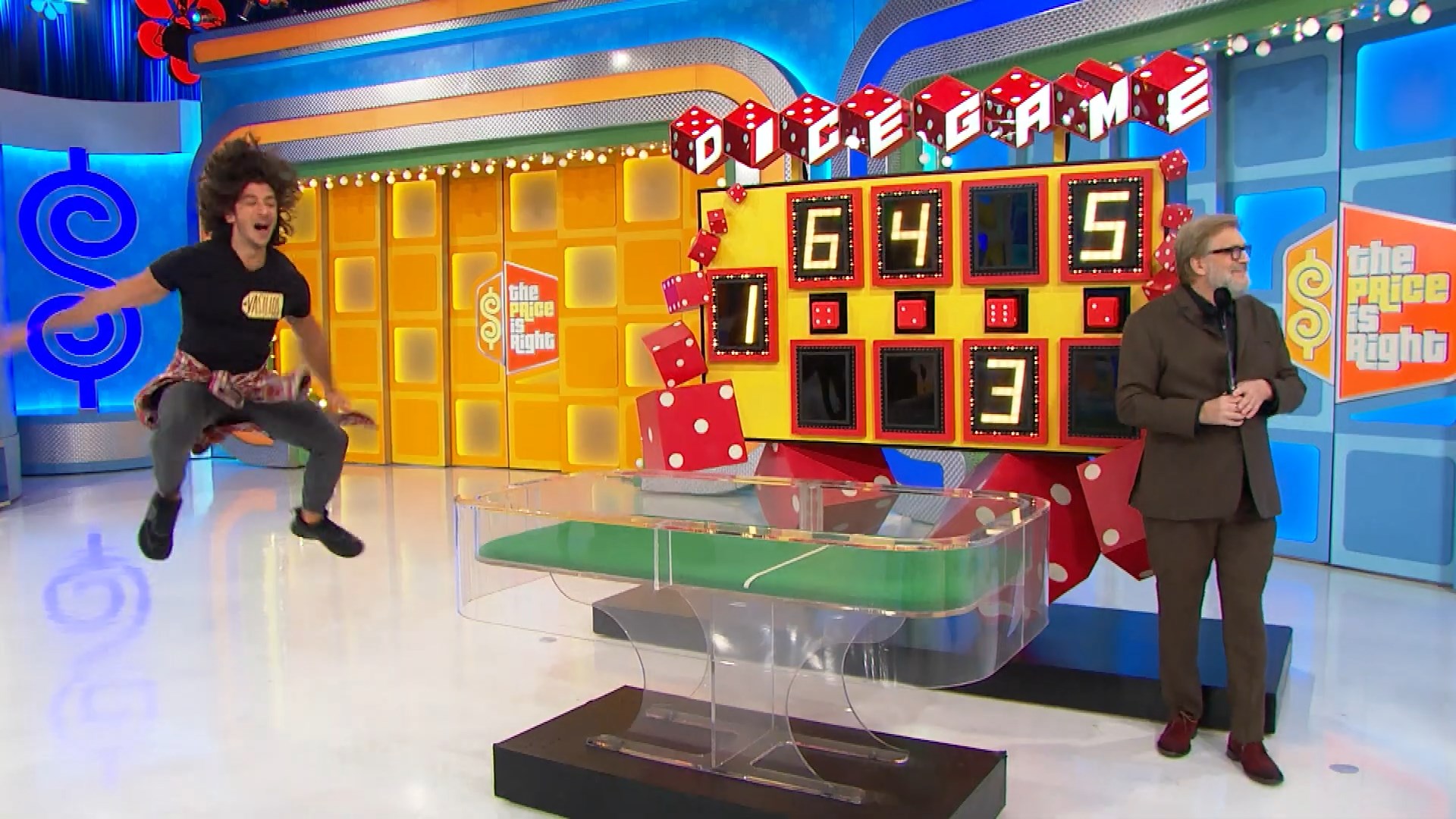 A contestant joyfully jumps in excitement during the Dice Game on 'The Price is Right,' with a colorful game board displaying numbers and oversized dice.