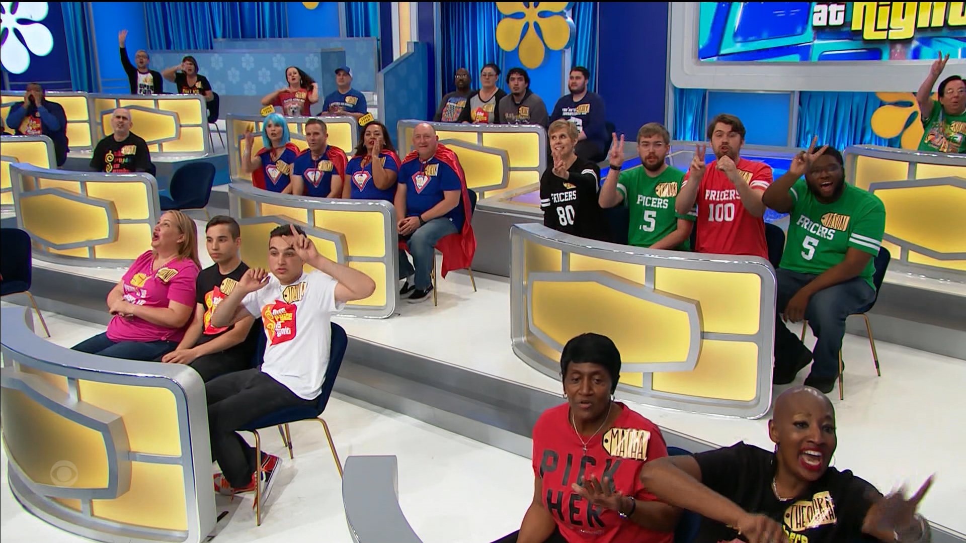 Audience members enthusiastically participating during a game show taping, wearing colorful team shirts and cheering.